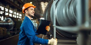 Worker with notebook, large turbine on background Male worker with notebook, large turbine on background, plant. Industrial production, metalwork engineering, machines manufacturing
